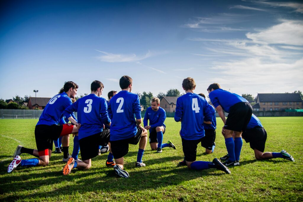 pexels-photo-262524-262524 A group of male football players in blue uniforms huddle on a grassy field before a match.